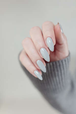Female hand with long nails light gray manicure and a bottle of nail polishの写真素材