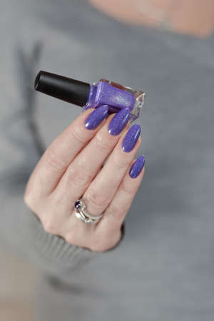 Female hand with long nails and a bottle of light blue lilac color nail polish