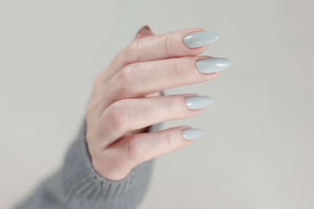 Female hand with long nails light gray manicure and a bottle of nail polishの写真素材