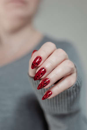 Female hand with long nails and a bright red manicure holds a bottle of nail polishの写真素材