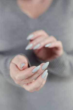 Female hand with long nails light gray manicure and a bottle of nail polishの写真素材