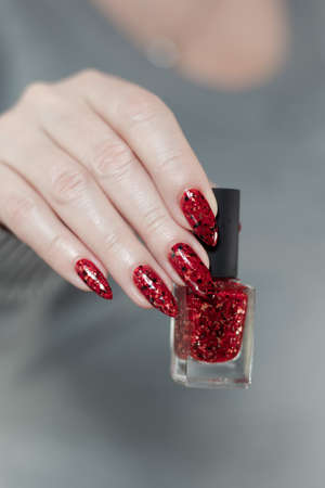 Woman's hands with long nails and a bottle of bright red nail polish