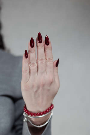 Female hand with long nails and a red manicure holds a bottle of nail polishの写真素材