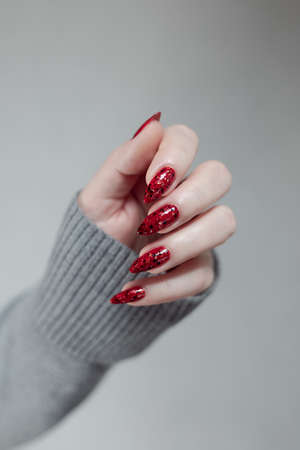 Female hand with long nails and a red manicure holds a bottle of nail polishの写真素材
