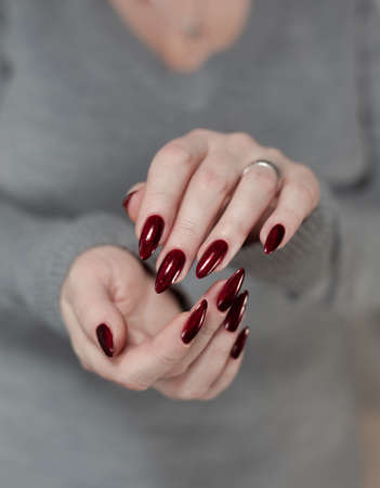Female hand with long nails and a red manicure holds a bottle of nail polishの写真素材