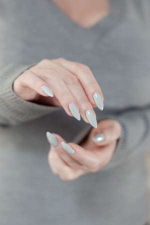 Female hand with long nails light gray manicure and a bottle of nail polish
