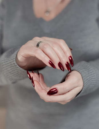 Woman's hands with long nails and a bottle of bright red nail polish