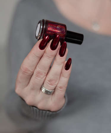 Woman's hands with long nails and a bottle of bright red nail polishの写真素材
