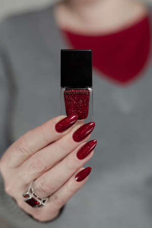 Female hand with long nails and a red manicure holds a bottle of nail polish