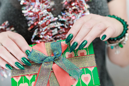 Female hands with long nails and bright green manicure hold a gift box.
