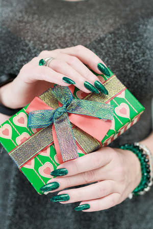 Female hands with long nails and green manicure hold a gift box for the holiday.