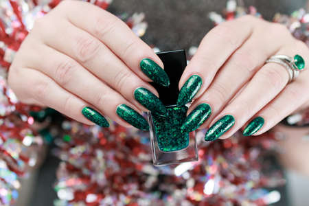Women's hands with long nails and bright green manicure. Congratulations to the New Year and...