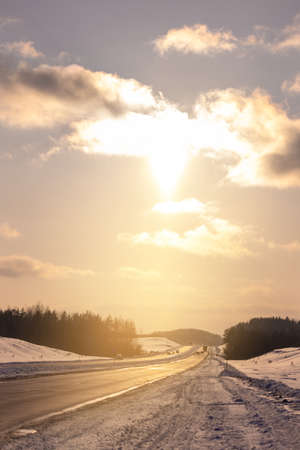 Winter road with snow, highway with cars at sunset on a sunny winter dayの写真素材