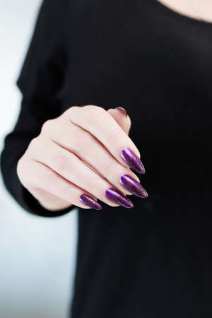 Female hand with long nails and purple plum manicure holds a bottle of nail polishの写真素材