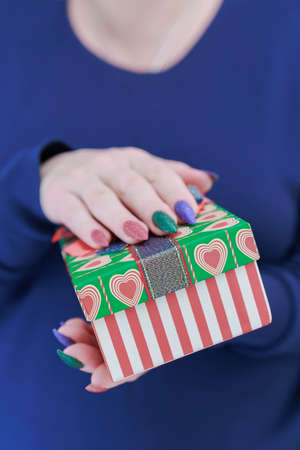 Female hands with long nails hold a gift box with a present for the holidays.