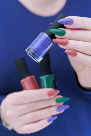 beautiful Woman's hands with long nails and multi-colored manicure, bottles of nail polishesの写真素材