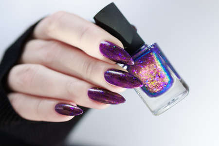 Female hand with long nails and purple plum manicure holds a bottle of nail polish