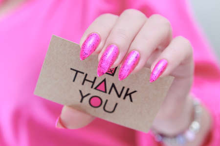 Female hands with long nails and neon pink nail polish hold a picture with the inscription Thank youの写真素材