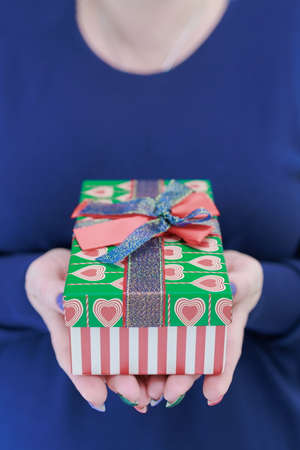 Female hands with long nails hold a gift box with a present for the holidays.