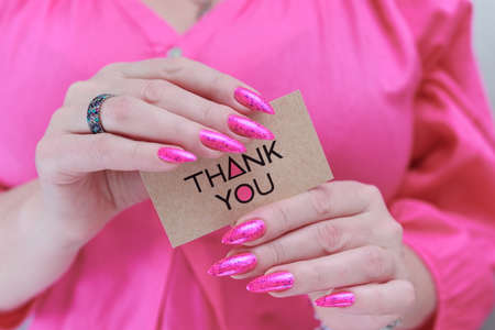 Female hands with long nails and neon pink nail polish hold a picture with the inscription Thank youの写真素材