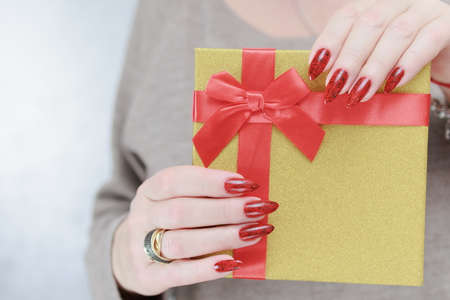 Female hands with long nails and red manicure hold a box with a gift for the holiday.の写真素材