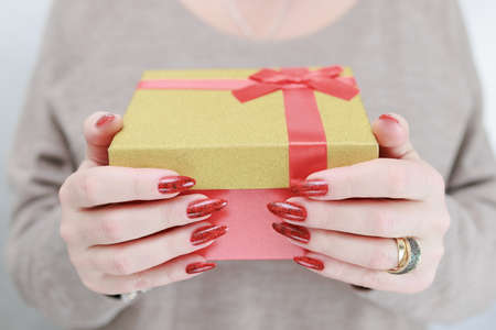 Female hands with long nails and red manicure hold a box with a gift for the holiday.
