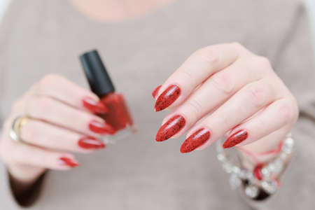Female hand with long nails and a red manicure holds a bottle of nail polish