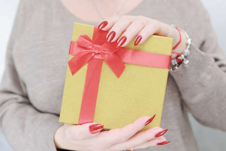 Female hands with long nails and red manicure hold a box with a gift for the holiday.の写真素材
