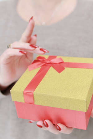 Female hands with long nails and red manicure hold a box with a gift for the holiday.の写真素材