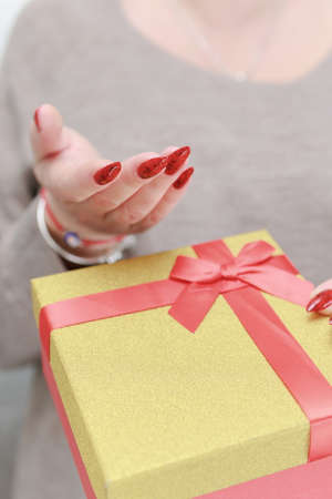 Female hands with long nails and red manicure hold a box with a gift for the holiday.