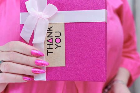 Female hands with long nails and neon pink nail polish hold a picture with the inscription Thank youの写真素材