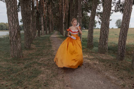 A young woman in an old orange dress walks on the shore of the lake near the castleの写真素材