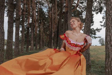 A young woman in an old orange dress walks on the shore of the lake near the castleの写真素材