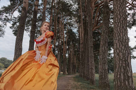 A young woman in an old orange dress walks on the shore of the lake near the castleの写真素材