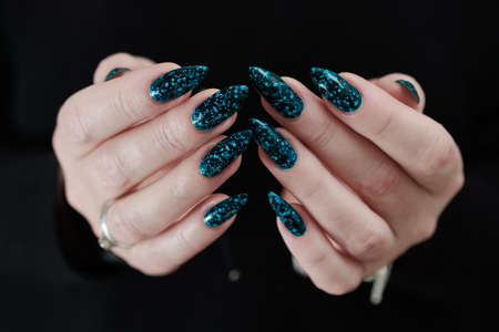 Woman's beautiful hand with long nails and turquoise green and blue manicure with bottles of nail...