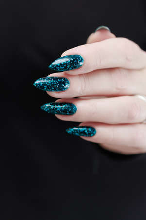 Woman's beautiful hand with long nails and turquoise green and blue manicure with bottles of nail...