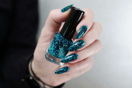 Woman's beautiful hand with long nails and turquoise green and blue manicure with bottles of nail...
