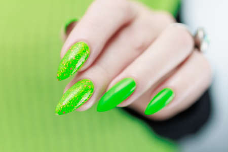 Female hand with long nails and neon green manicure with bottles of nail polishの写真素材