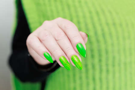 Female hand with long nails and neon green manicure with bottles of nail polishの写真素材