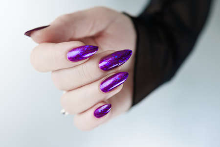Female hand with long nails and purple blue manicure holds a bottle of nail polishの写真素材