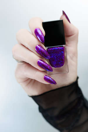 Female hand with long nails and purple blue manicure holds a bottle of nail polish