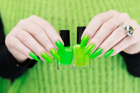 Female hand with long nails and neon green manicure with bottles of nail polishの写真素材