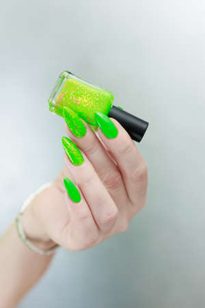 Female hand with long nails and neon green manicure with bottles of nail polish