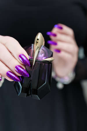 Female hand with long nails and purple blue manicure holds a bottle of nail polish
