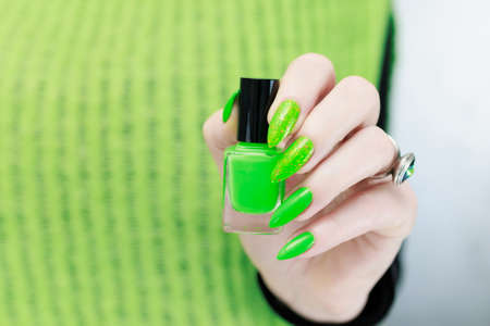 Female hand with long nails and neon green manicure with bottles of nail polishの写真素材