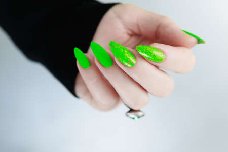 Female hand with long nails and neon green manicure with bottles of nail polishの写真素材