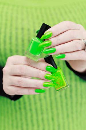Female hand with long nails and neon green manicure with bottles of nail polishの写真素材