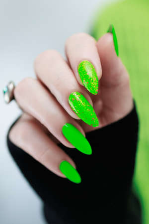Female hand with long nails and neon green manicure with bottles of nail polishの写真素材
