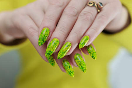 Female hand with long nails and neon green manicure with bottles of nail polish