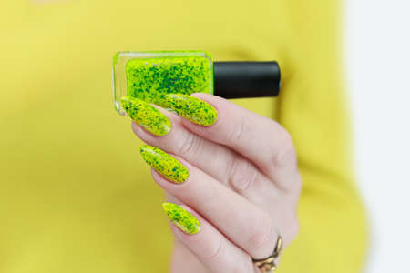 Female hand with long nails and neon green manicure with bottles of nail polishの写真素材